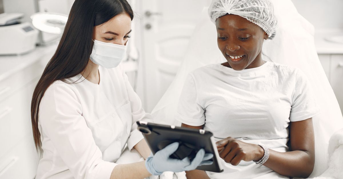 Smiling patient and dermatologist using tablet during skincare consultation.